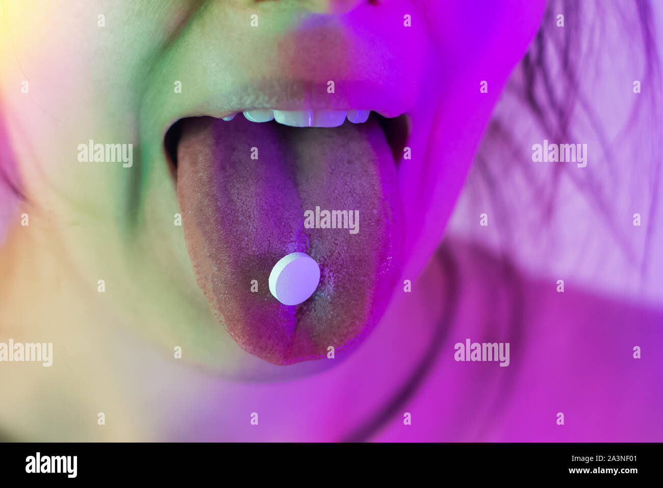 Weibliche Zunge mit einer Pille auf es Close-up im Neonlicht. Die Einnahme von Drogen im Nachtclub. Stockfoto