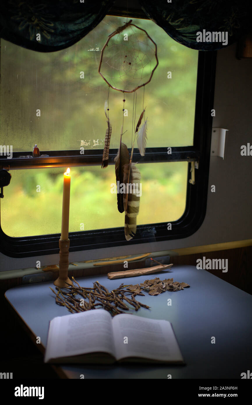 Eine einfache handgefertigte Traumfänger dekorieren Fenster einer Camper Trailer, leuchtet eine Kerze, eine Philosophie Buch und einige Trocknen von Pilzen und Wurzeln Stockfoto