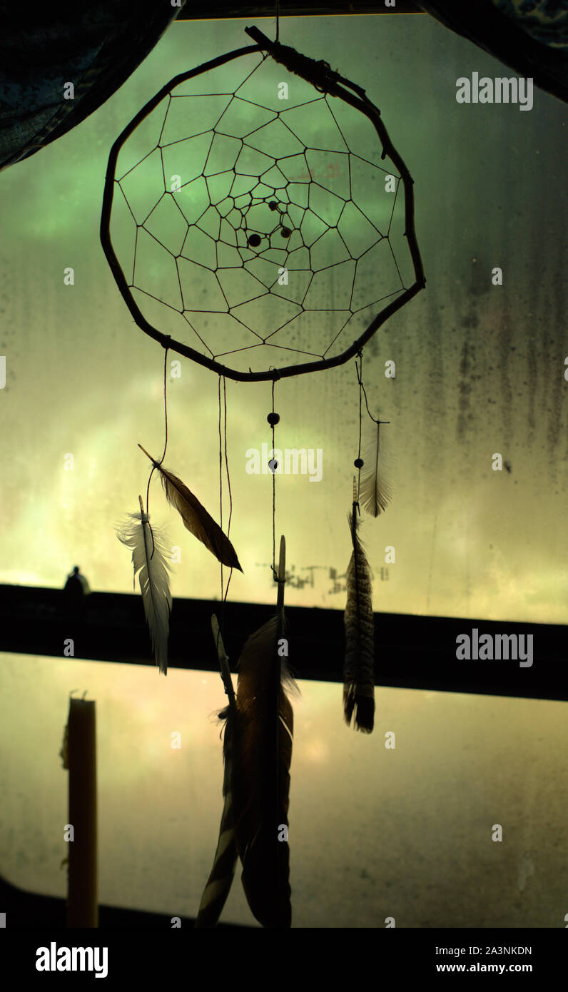 Eine einfache handgefertigte Traumfänger Dekorieren ein Fenster, mit dunklen Farben im Kontrast zu den grünen und gelben verschwommenen Hintergrund Stockfoto