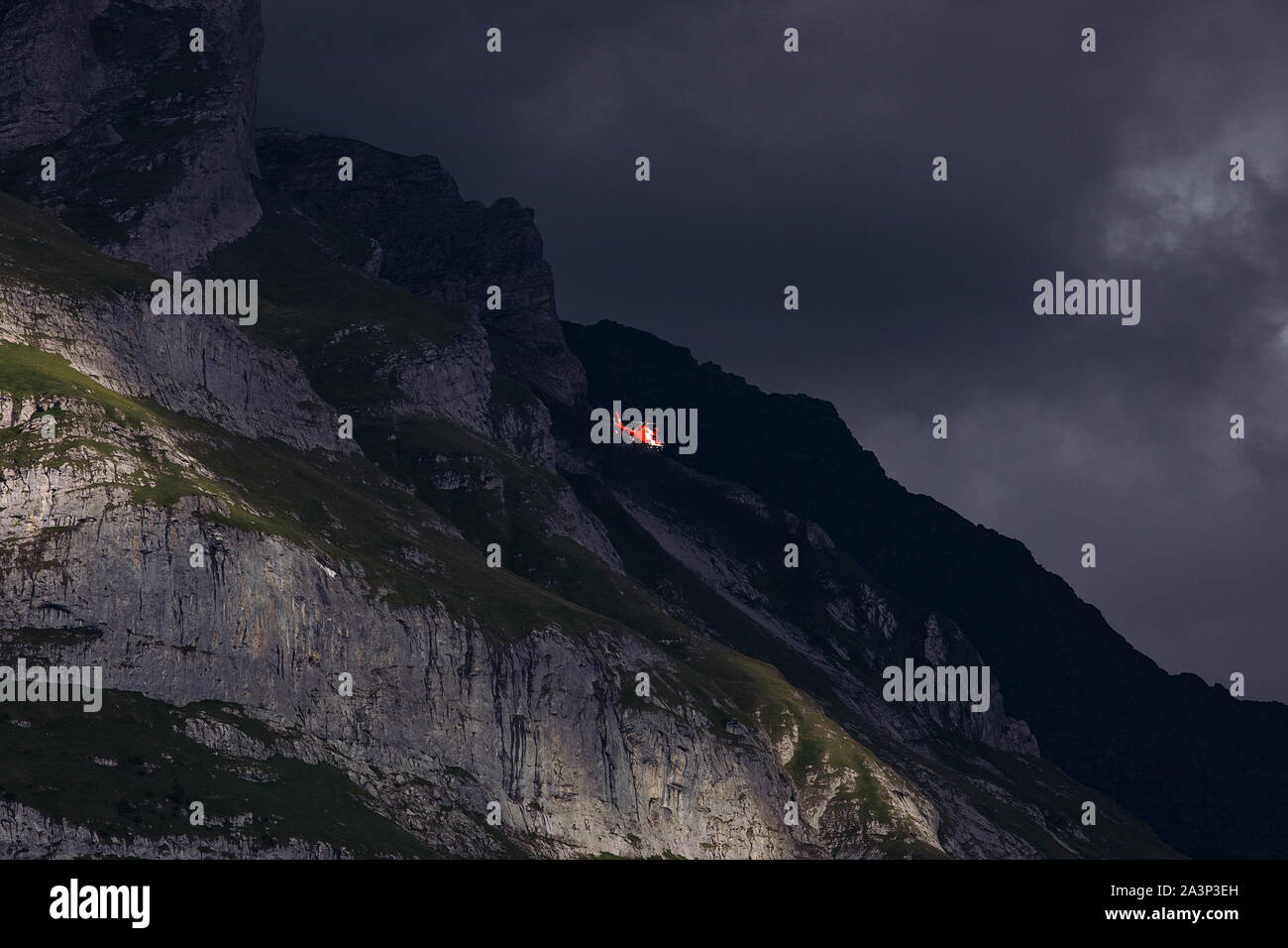 Rote Helikopter auf dem Hintergrund der massiven dunklen Berg. Bewölkten Himmel. Rettungshubschrauber in Berge, Dämmerung. Swiss Alpine Berge. Die Schweiz. Stockfoto