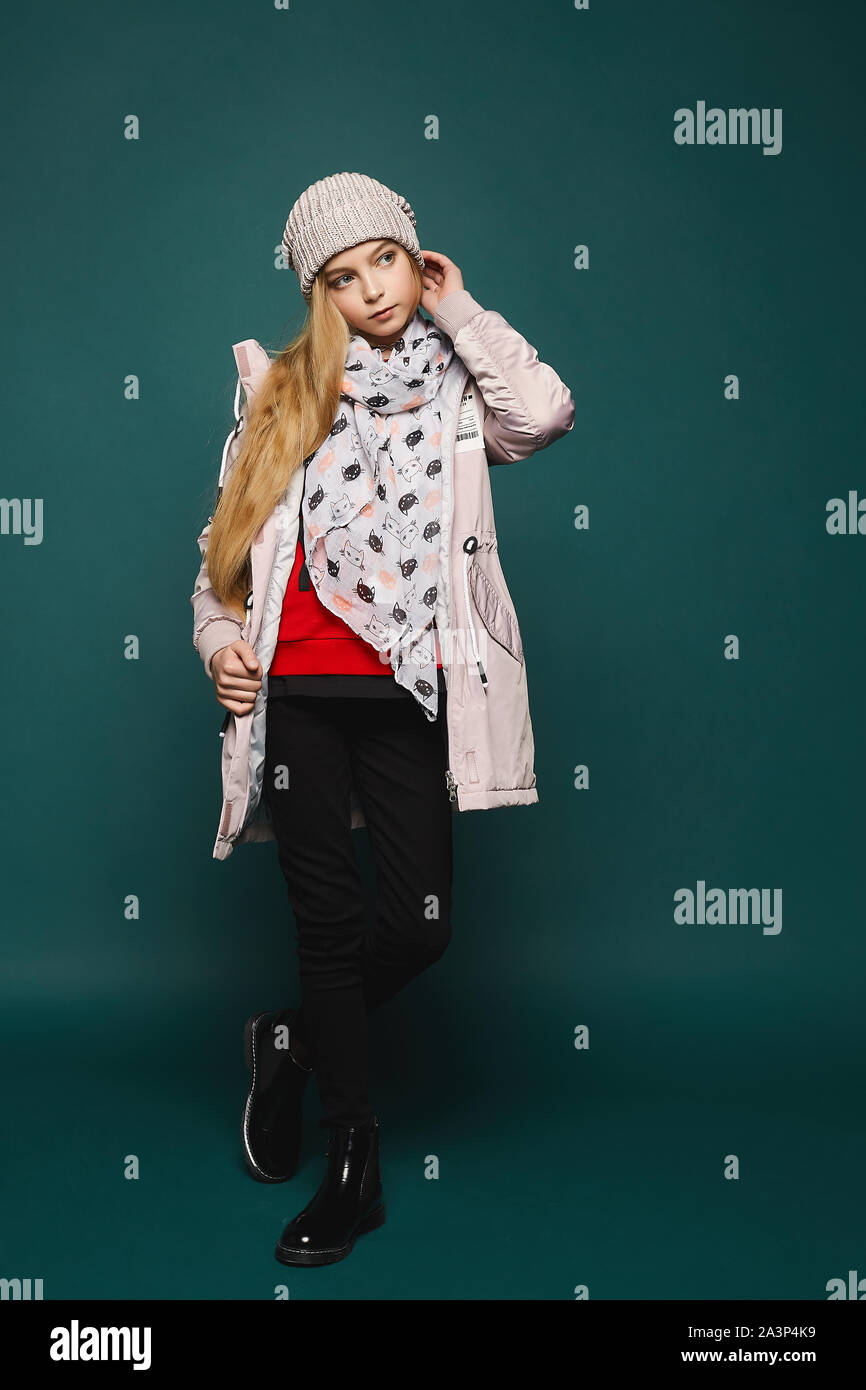 Ein Teenager blonden Model Mädchen in modische Winterbekleidung über den dunklen Hintergrund in voller Länge darstellen. Glückliches Mädchen tragen in Jeans, Stiefel, eine warme Jacke Stockfoto