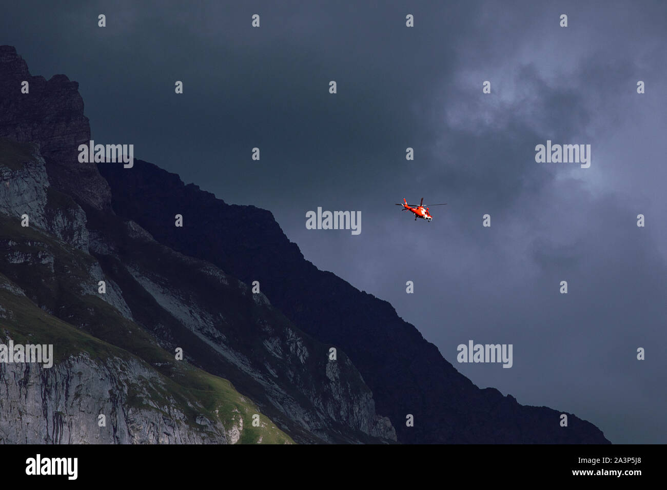 Rote Helikopter auf dem bewölkten Himmel Hintergrund. Großen Dunklen Berg. Rettungshubschrauber in den Rocky Mountains, Dämmerung. Swiss Alpine Berge. Schweiz Stockfoto