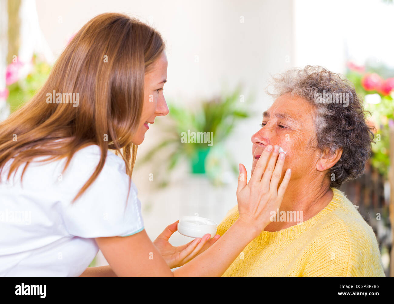 Betreuer reibt sich das Gesicht Creme auf die älteren womans Gesicht Stockfoto