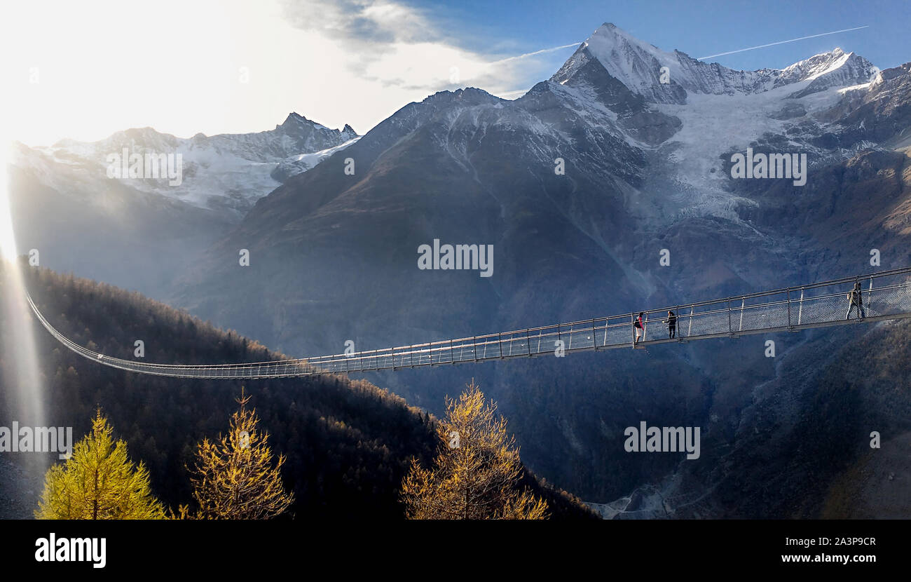 Randa, Schweiz, 8. Oktober 2019: lange Hängebrücke in Zermatt über Landschaft verschneite Berge Wald bei Sonnenuntergang. Suspension Bridge. Lange Brücken. Stockfoto