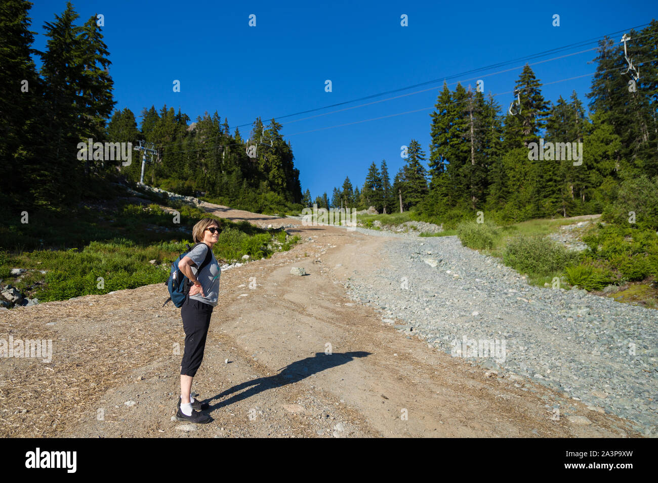 Eine Frau mittleren Alters zu Fuß auf einem Berg Wald Wanderweg mit Blick auf eine Stadt. Stockfoto
