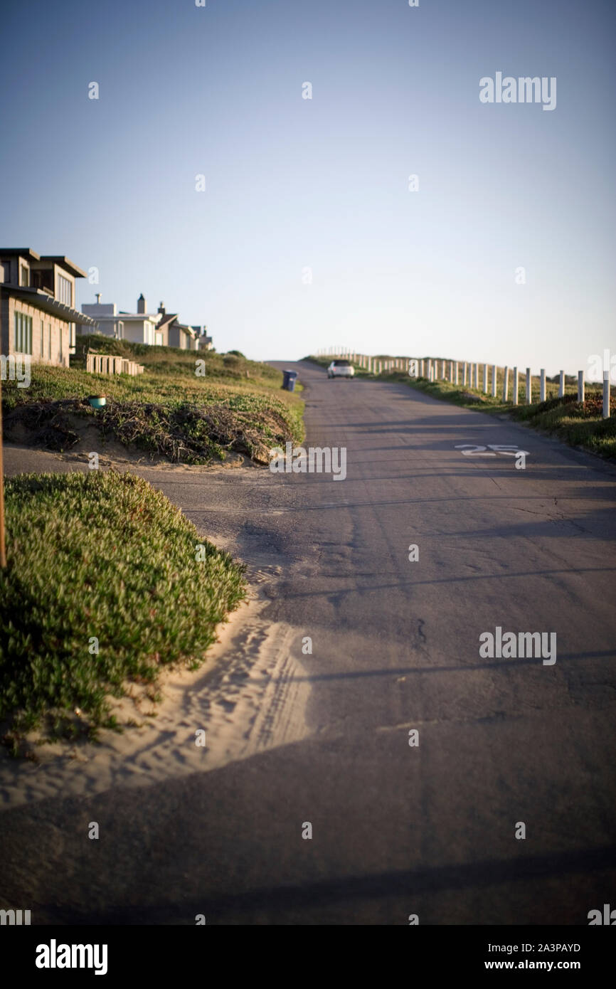 1-spurige Straße neben einer ländlichen Stadt am Meer, an einem sonnigen Tag. Stockfoto