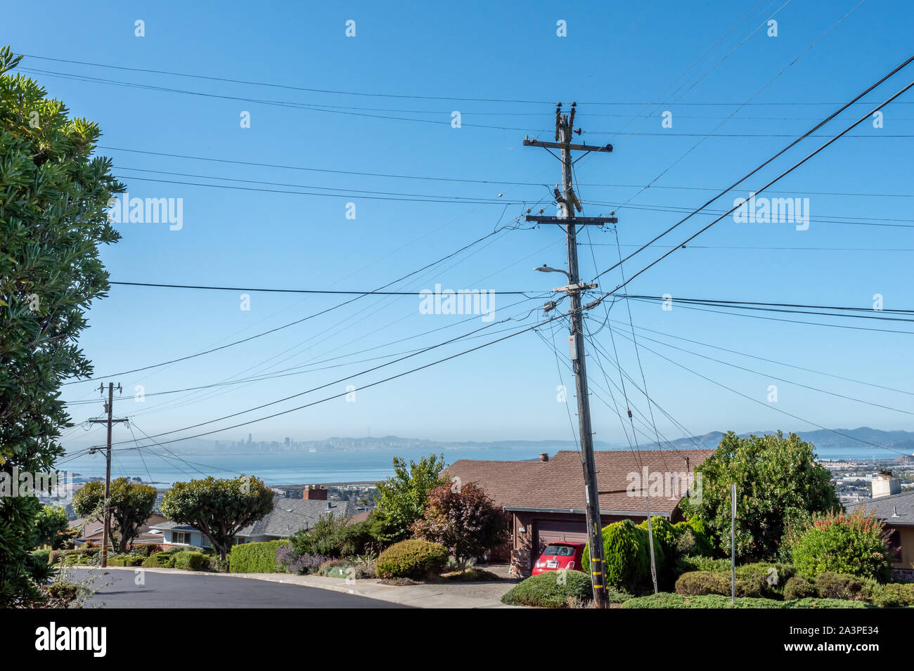 PG&E-Leitungen und Kabel schneiden sich an einem Strommast in El Cerrito, Kalifornien, Nachbarschaft. San Francsico Bucht und die Innenstadt sind in der Ferne. Stockfoto