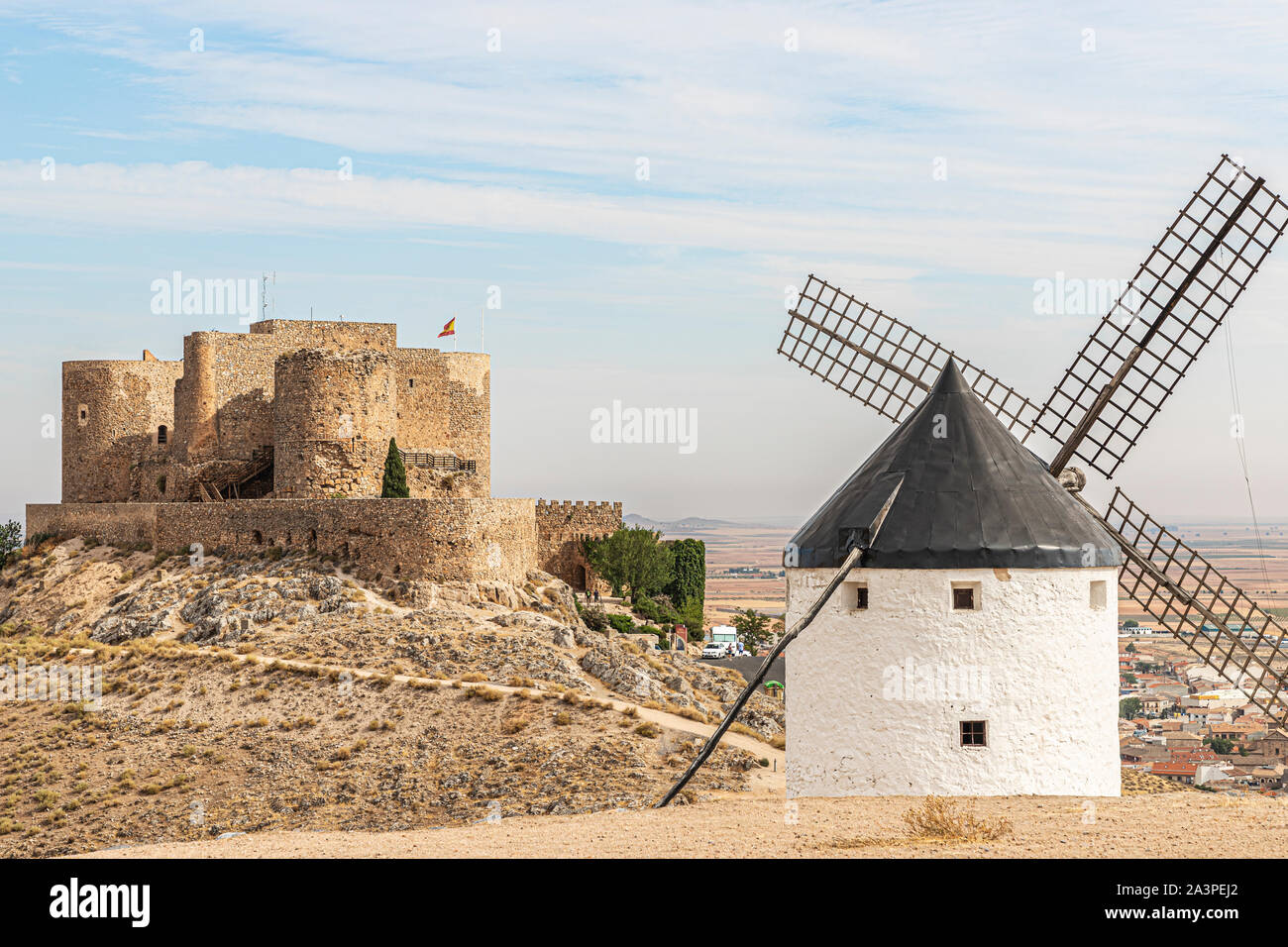 Landschaft in der spanischen Gemeinde Consuegra mit einer alten Mühle und das Schloss von La Muela im Hintergrund an einem Sommertag mit bewölktem Himmel Stockfoto