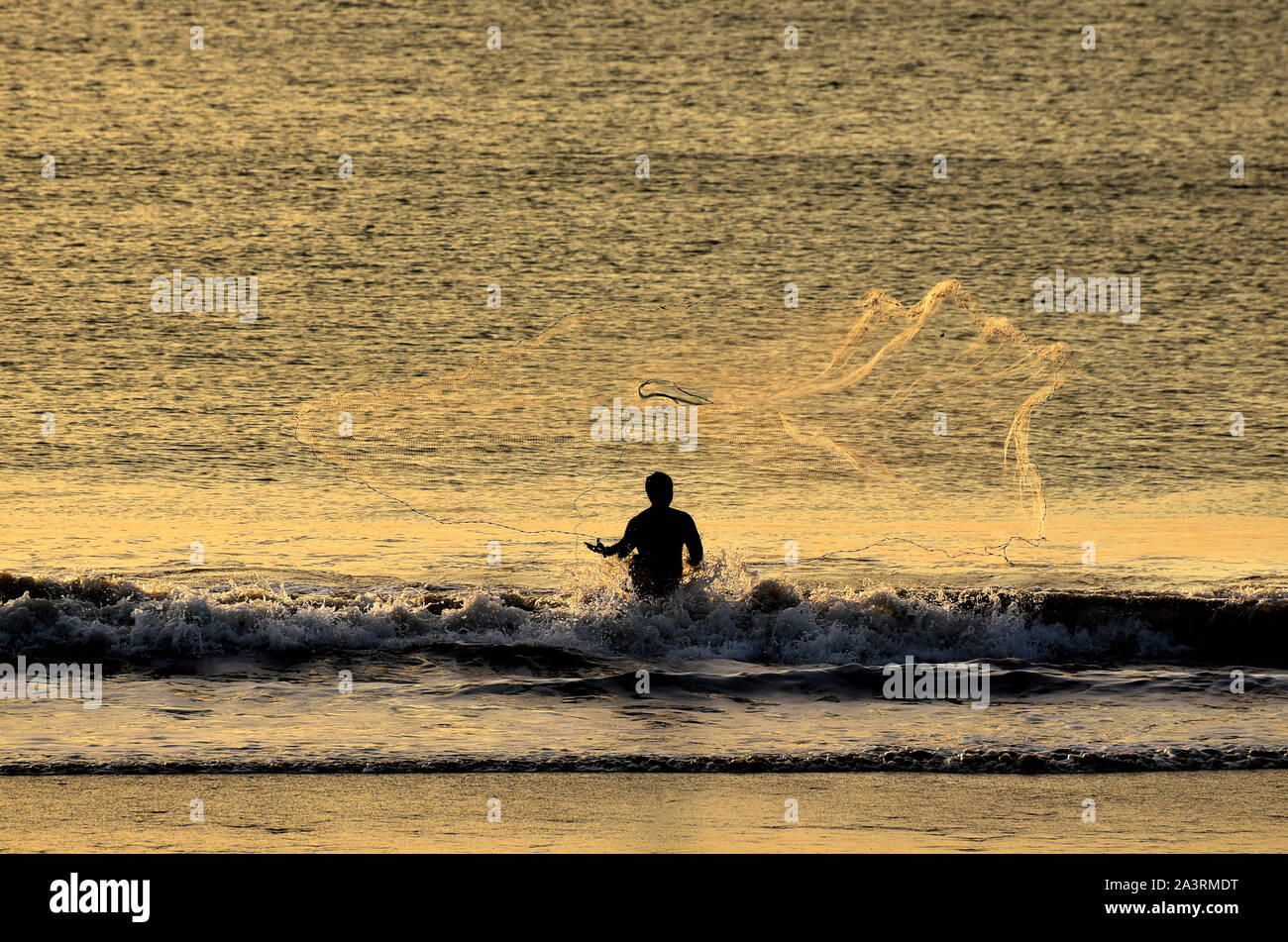 Fischerman warf einen Net am Jimbaran Strand bei Sonnenuntergang. Bali, Indonesien Stockfoto