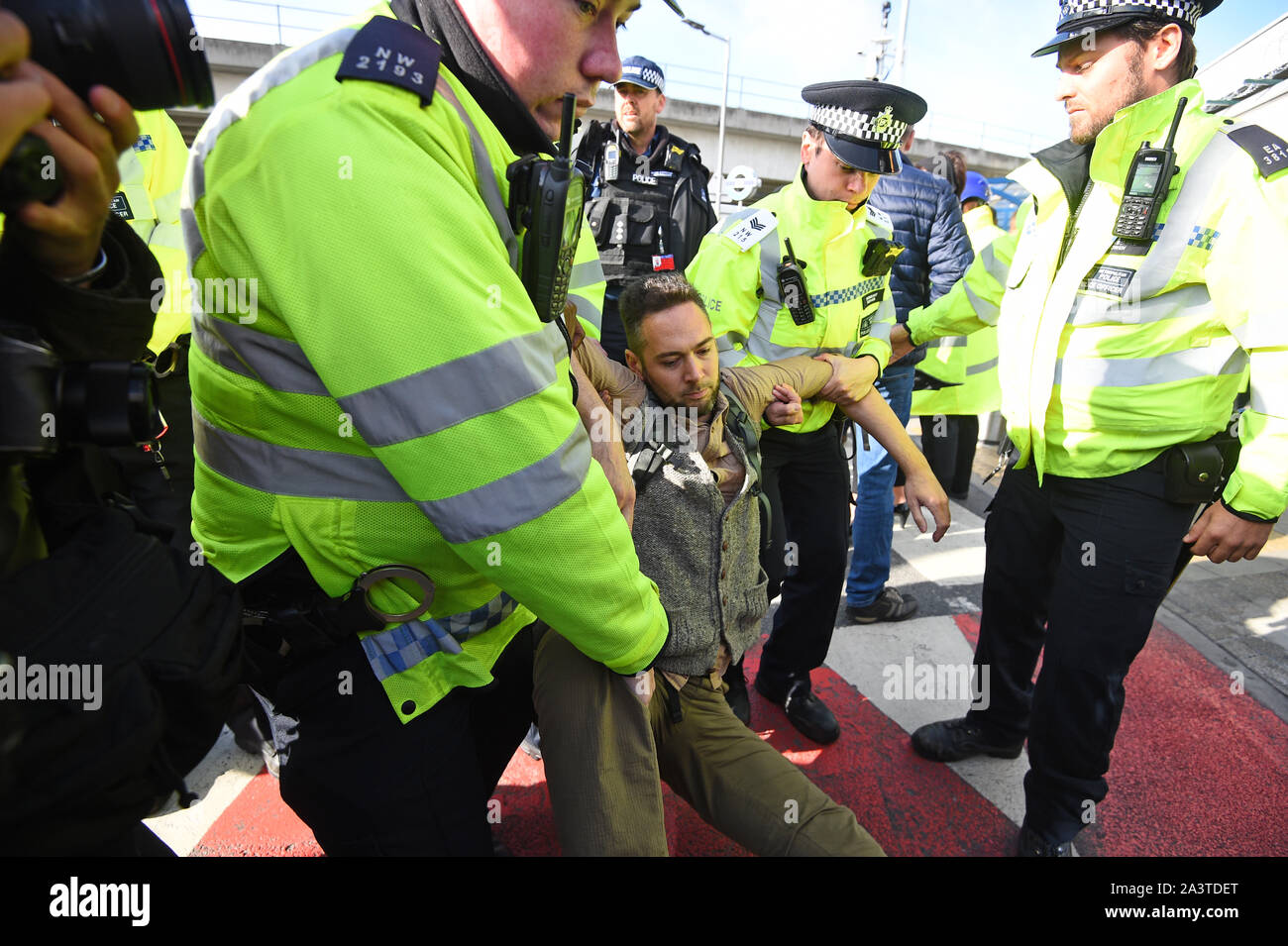 Ein Mann wird von der Polizei entfernt, nachdem Aktivisten einen "Hongkong" Stil der Sperrung der Ausfahrt aus dem Bahnhof zum City Airport, London inszeniert, während ein Aussterben Rebellion Klimawandel protestieren. Stockfoto