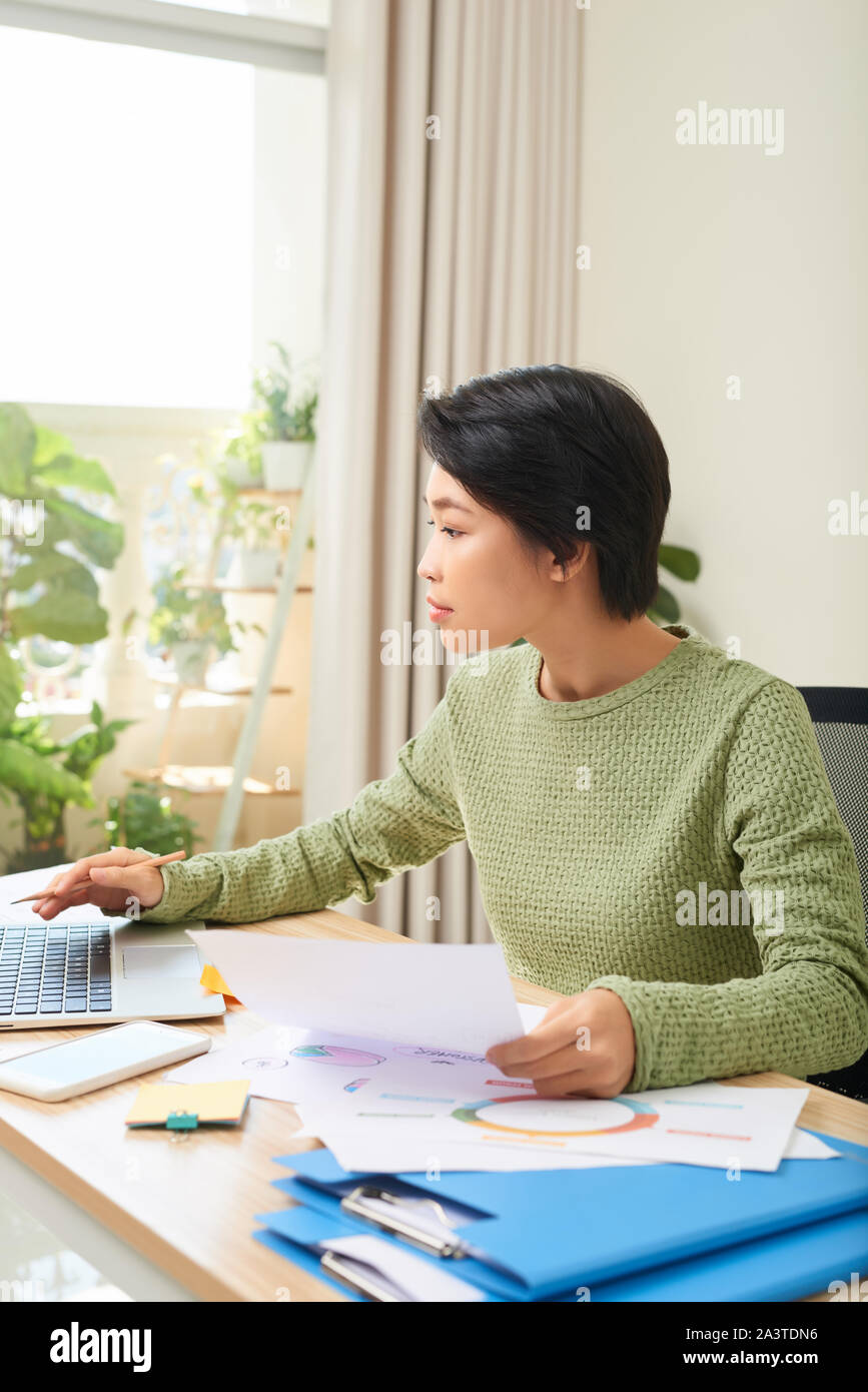 Konzentriert asiatische Frau sitzen am Tisch Arbeiten am Laptop Notizen in Notebook zu Hause Büro Stockfoto