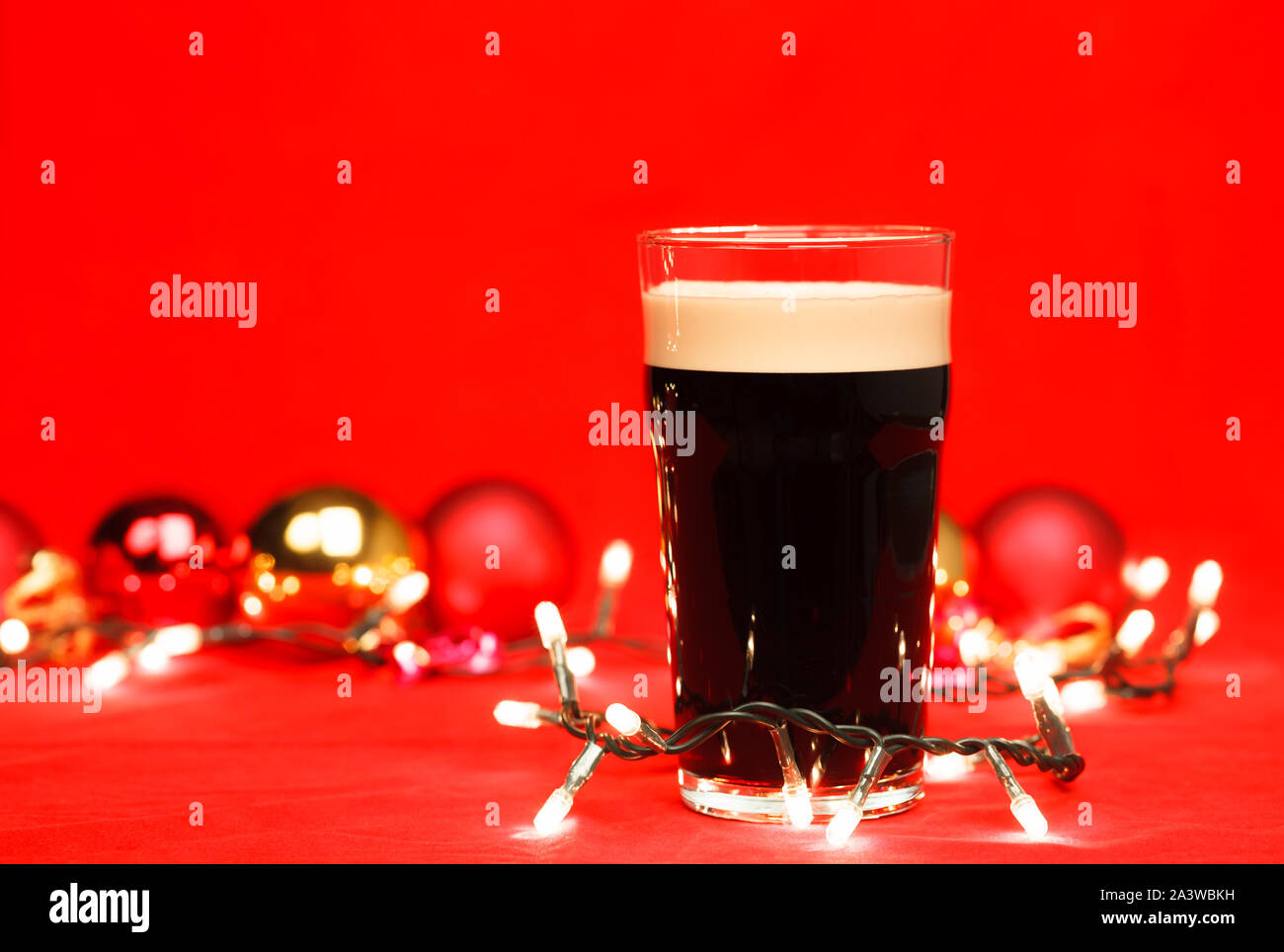 Pint Glas dunkles Bier oder stout Ale mit Weihnachten Lichter und Kugeln auf rotem Hintergrund Stockfoto