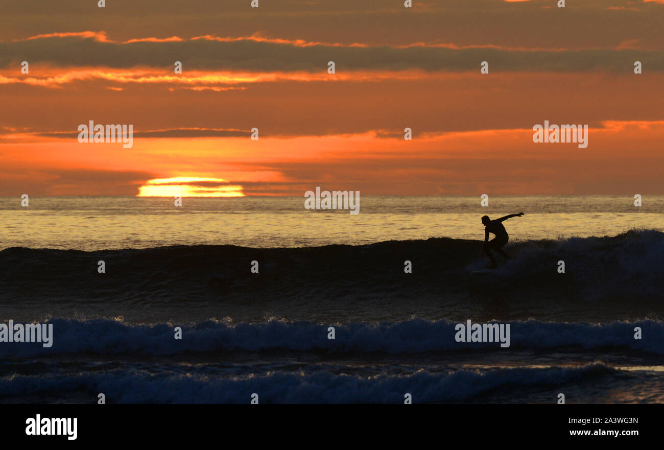 Ein Surfer silhouetted gegen die untergehende Sonne, wie Sie eine Welle an Barvas Bay fahren, auf der atlantischen Küste der Insel Lewis, Schottland. Stockfoto