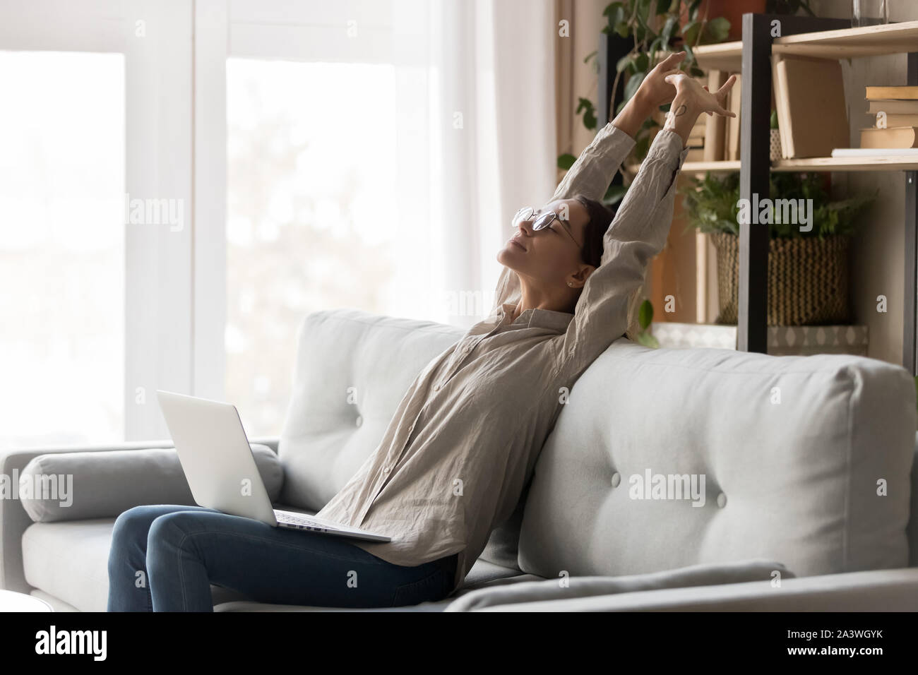 Glückliche Frau stretching sitzen auf komfortablen Couch mit Laptop Stockfoto