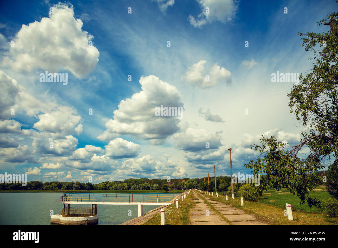 Konkrete Bahndamm entlang der See auf einem Sommer sonnigen Tag. Landschaft mit See und schönen Himmel Stockfoto