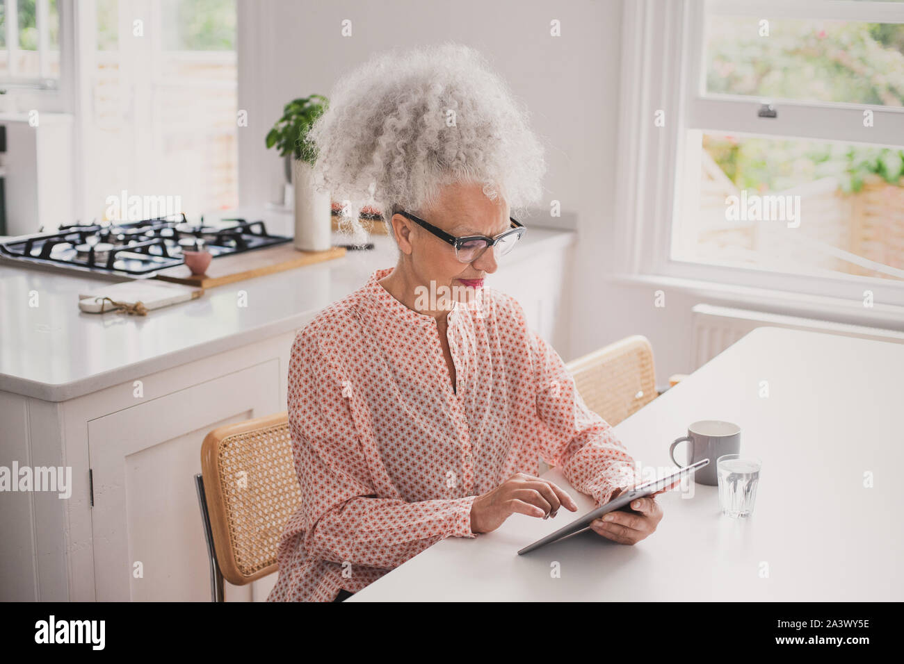 Ältere Erwachsene Frau am digitalen Tablet während Sie sich morgens Kaffee suchen Stockfoto
