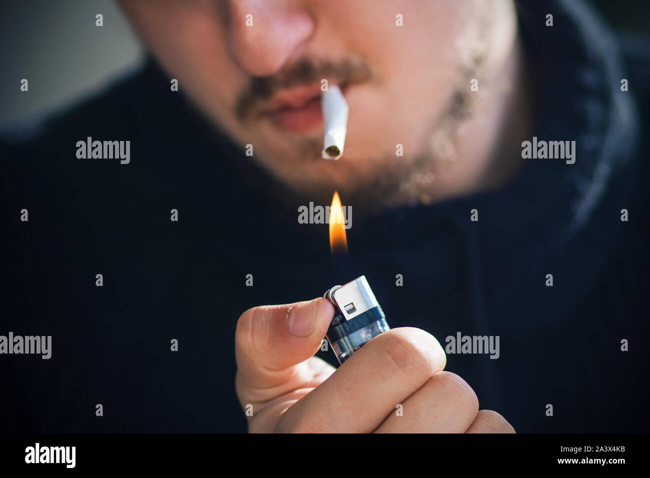 Ein bärtiger Mann in schwarzer Kleidung brennt eine Zigarette im Mund mit einem gasfeuerzeug. Stockfoto