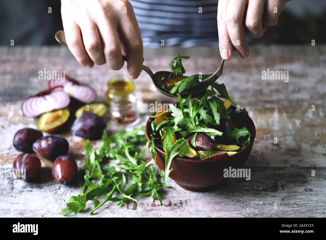 Männliche Hände gemischter Salat in eine Schüssel mit Löffel und Gabel. Leichten Salat mit Ruccola und Pflaumen. Herbst pflaume Salat. Gesundes Essen. Selektive konzentrieren. Makro. Stockfoto