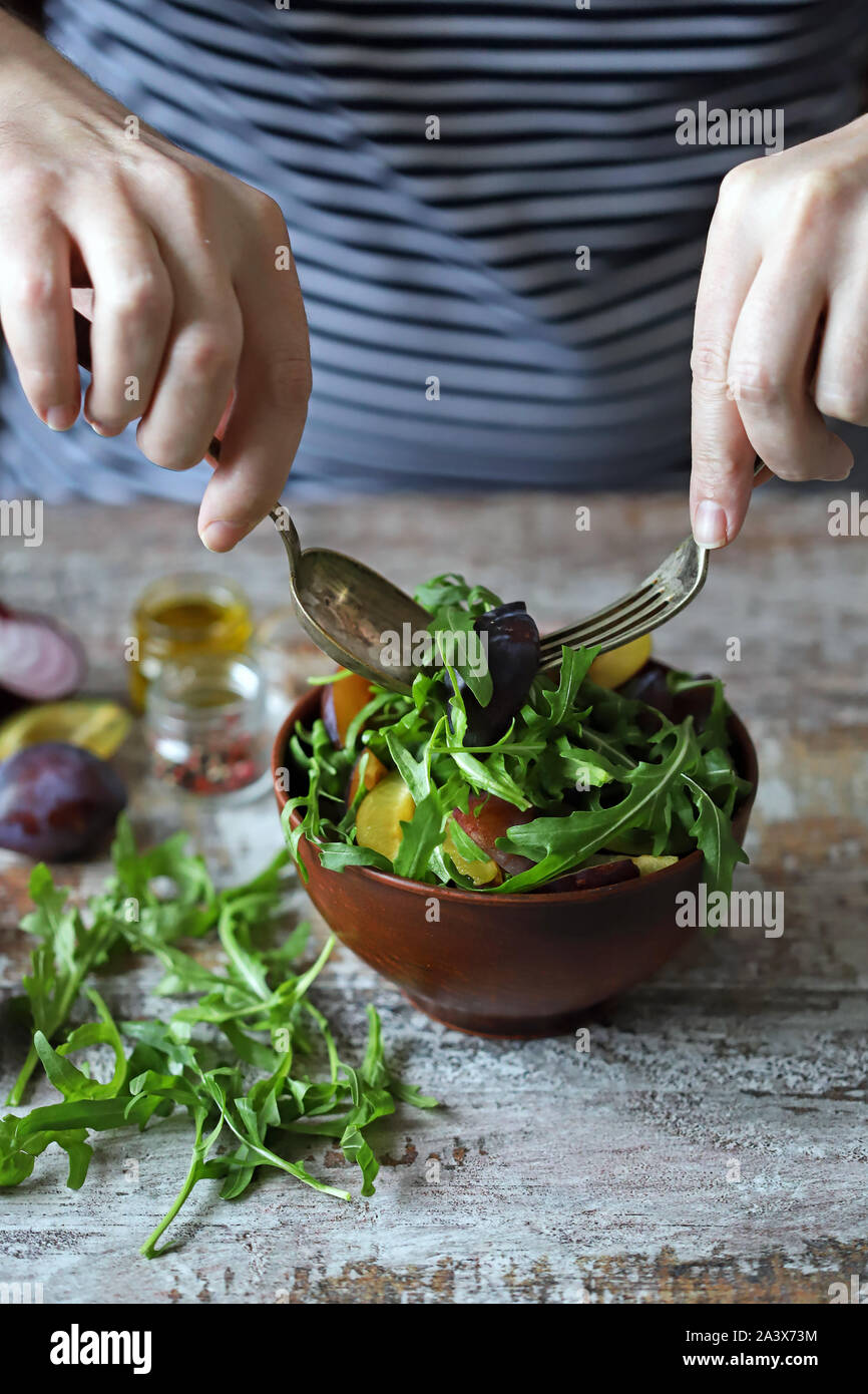 Männliche Hände gemischter Salat in eine Schüssel mit Löffel und Gabel. Leichten Salat mit Ruccola und Pflaumen. Herbst pflaume Salat. Gesundes Essen. Selektive konzentrieren. Makro. Stockfoto