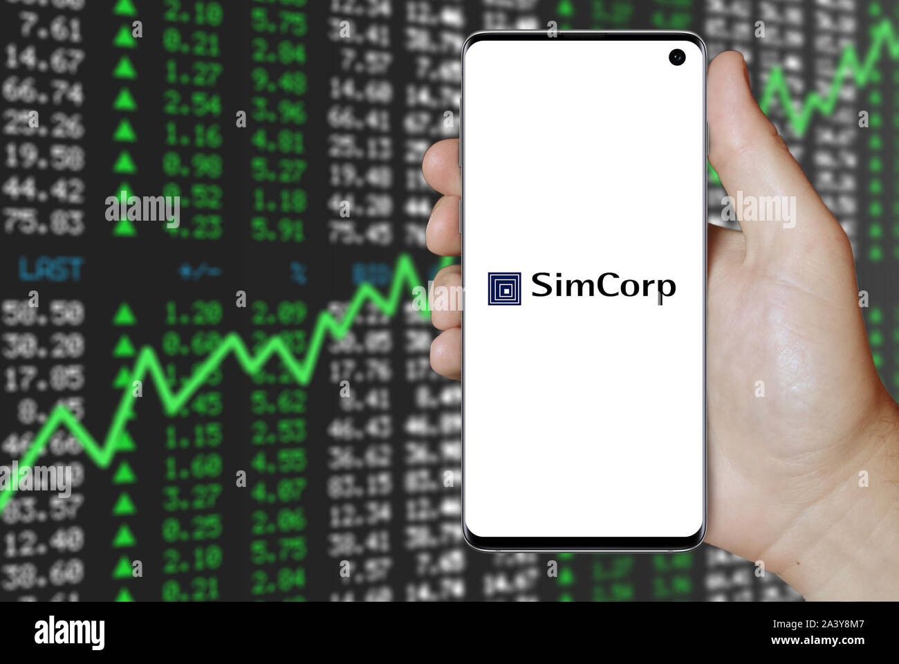 Ein Mann hält ein Telefon mit dem Logo der Firma SimCorp aufgeführt im OMX Kopenhagen. Positive Börse. Credit: PIXDUCE Stockfoto