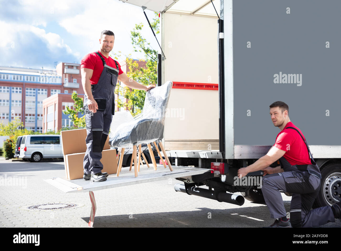 Zwei junge männliche Movers laden die Kartons und Möbel in Umzugs-LKW auf der Straße Stockfoto