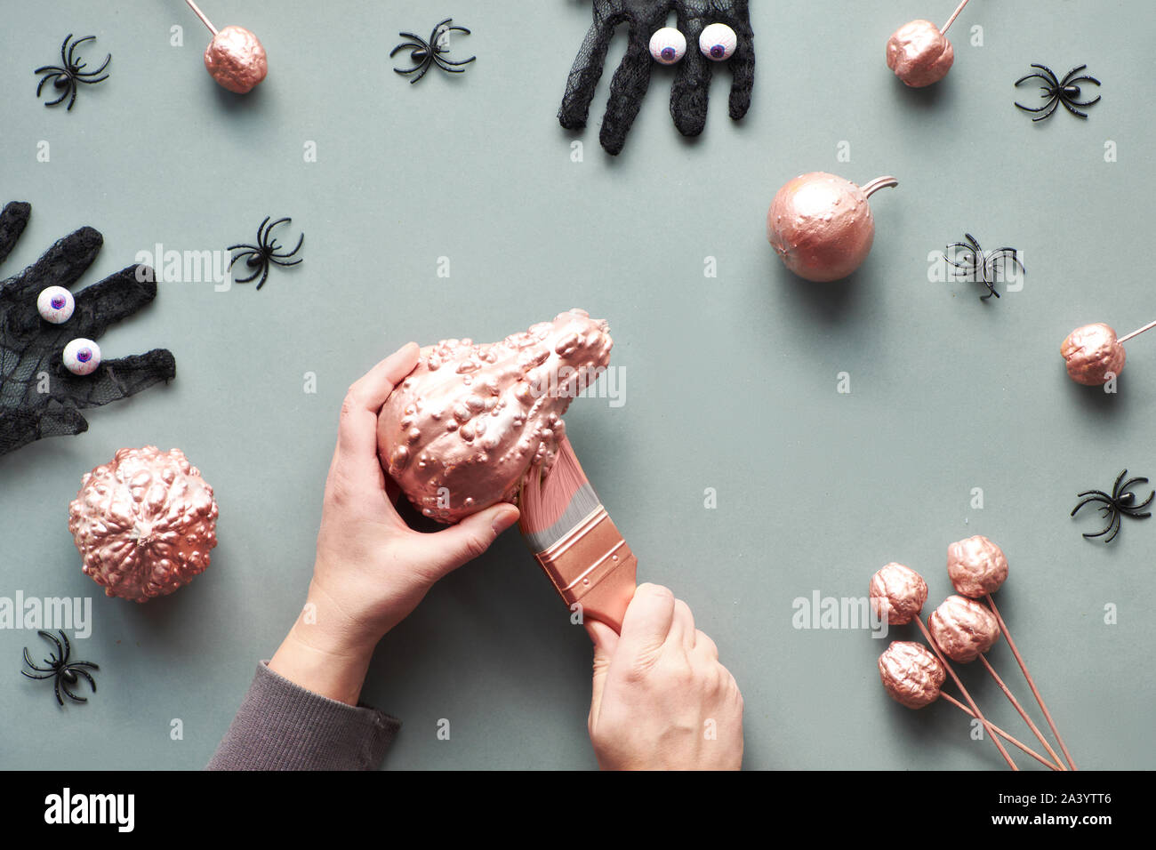 Kreative grau und rosa Papier flach mit Händen Malerei Kürbis mit Metallisch Rosa glitzernden malen. Ansicht von oben mit Gitter Handschuhe mit Schokolade Augen, Stockfoto