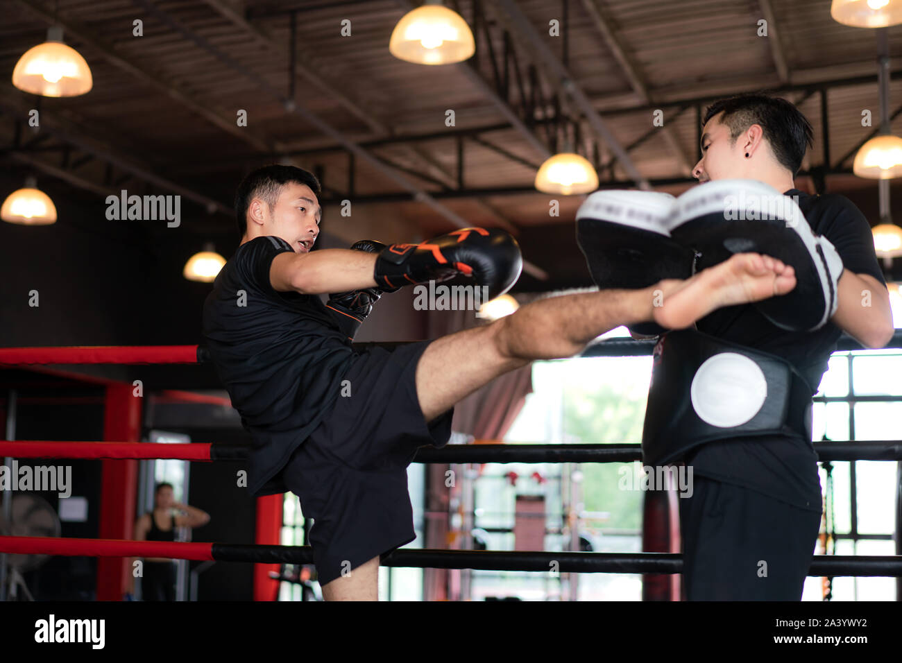 Jungen asiatischen Kick Boxer treten professionelle Trainer im Boxen studuim im Hintergrund bei Fitness Gym. Boxer schlagen die Sandsack für Bodybuilding Stockfoto