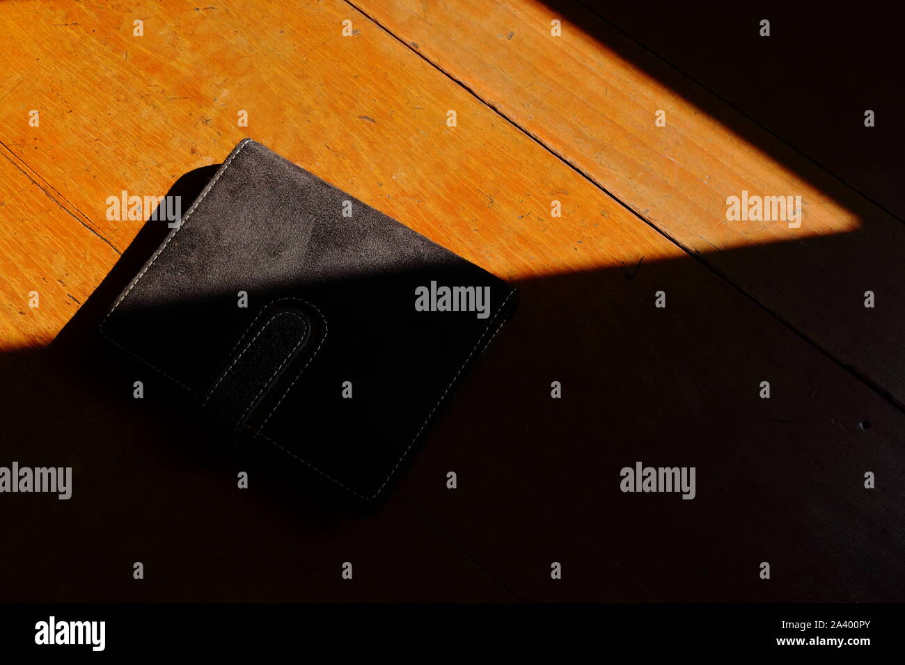 Nahaufnahme von einer geschlossenen Black Book auf hölzernen Tisch unter Sonneneinstrahlung ausgesetzt, schwarzes Buch Konzept Stockfoto