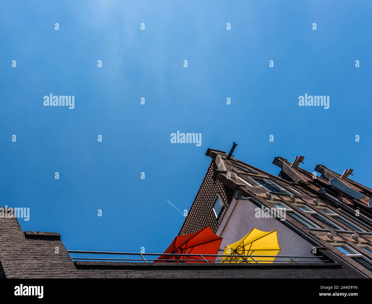 Die roten und gelben Sonnenschirmen auf einem hohen Balkon gegen den blauen Himmel und ein Flugzeug fliegen über echten High Stockfoto