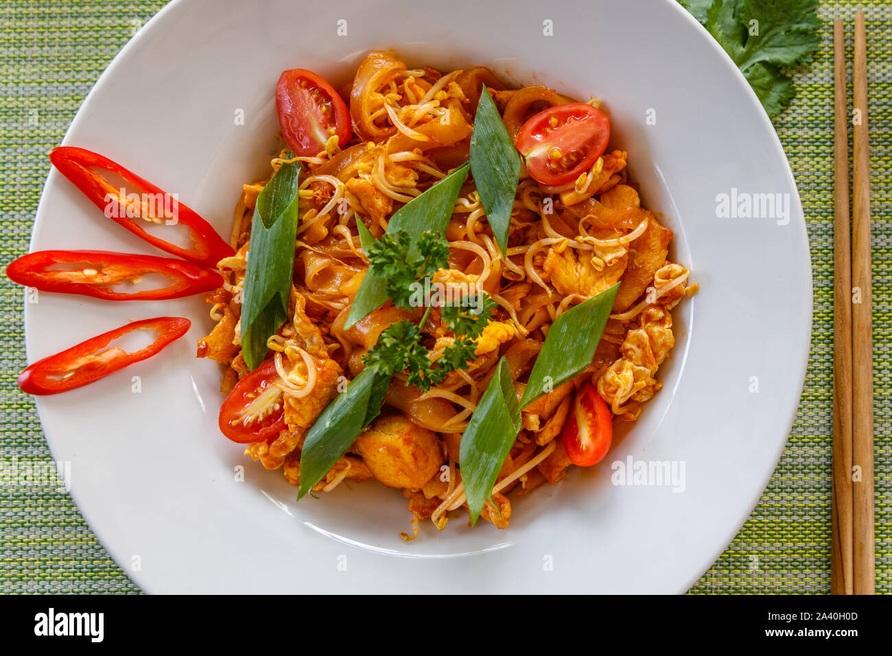 Traditionelle thailändische Nudelgericht Pad Thai mit Huhn auf weißer Keramik Teller serviert. Ansicht von oben. Mit Stäbchen auf der Seite. Grüner Hintergrund. Stockfoto