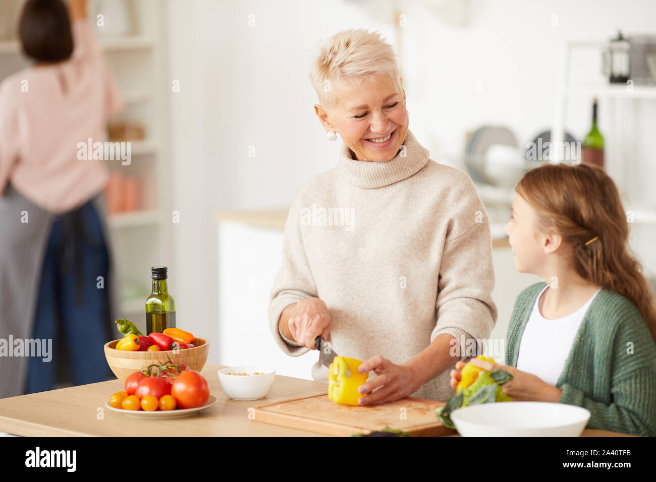 Gerne schöne Großmutter Schneiden von Gemüse und lächelnd zu ihrer Enkelin, die ihr hilft in der Küche zu kochen Stockfoto