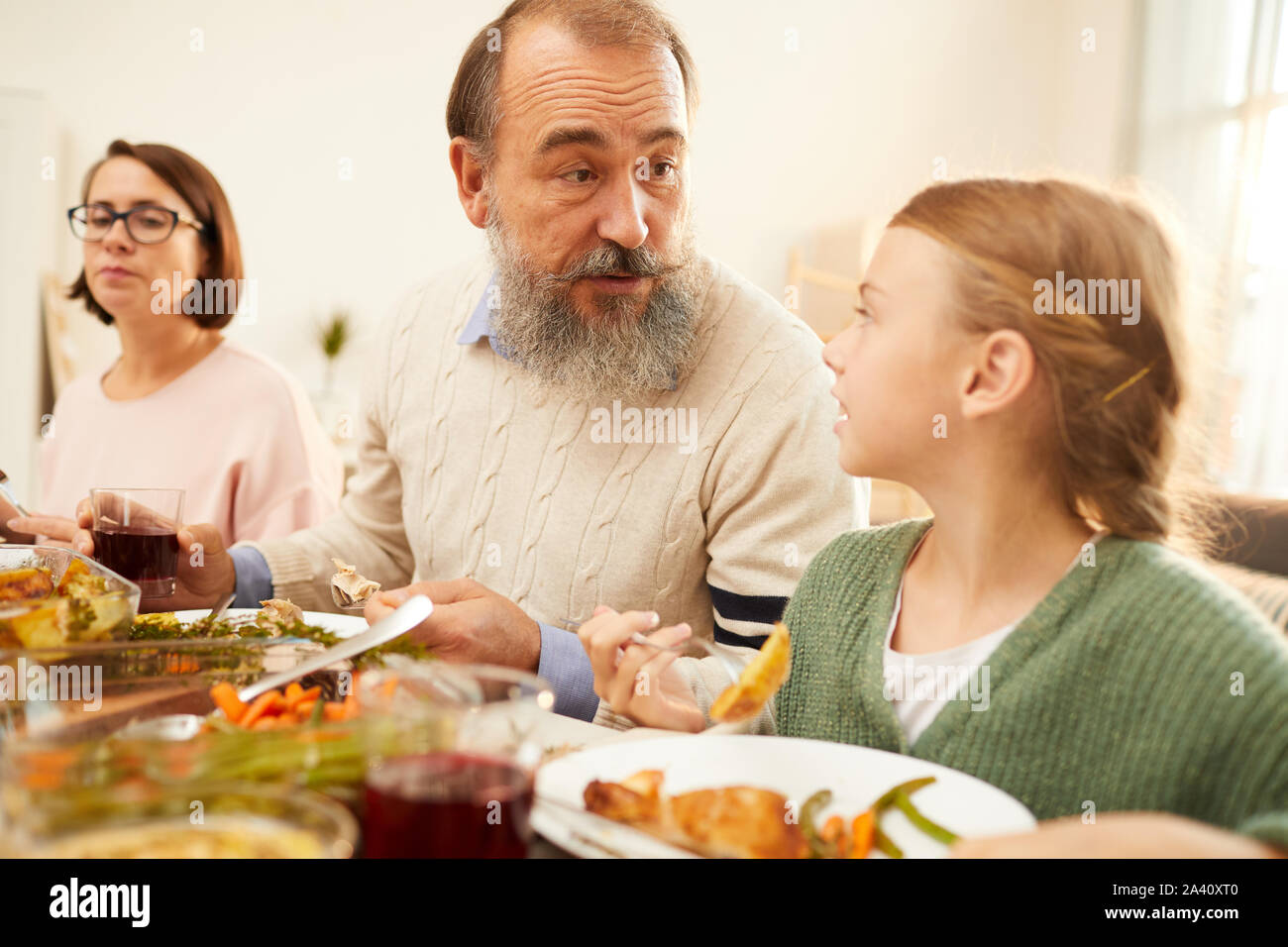 Großvater seine Enkelin zu reden, während Sie das Abendessen am Tisch mit anderen Mitgliedern der Familie zu Hause haben Stockfoto