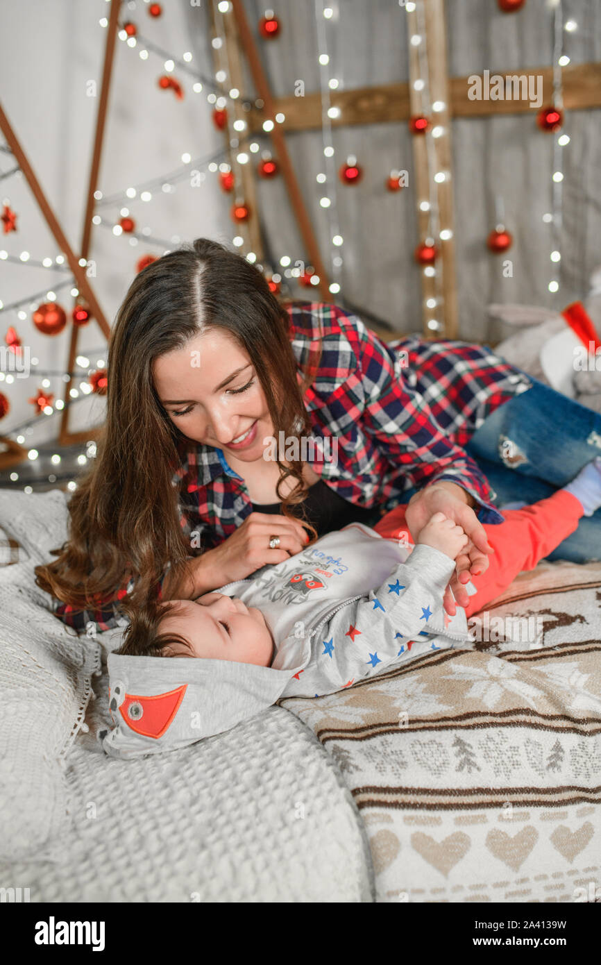 Junge Mutter mit Kind in ein neues Jahr. Weihnachten Familie, Mutter und Kind lächeln in der Nähe der Weihnachtsbaum. Das Wohnzimmer ist eingerichtet Stockfoto