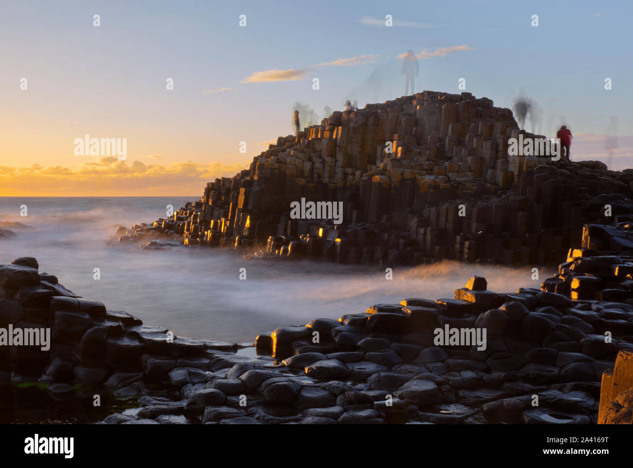 Lange Belichtung Sonnenuntergang am Giant's Causeway mit Schatten von sich bewegenden Personen stehend auf Felsen Erstellen eines Ghost Wirkung Stockfoto