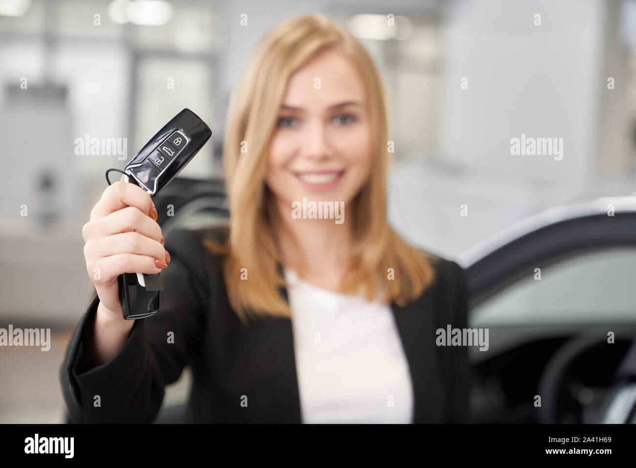 Selektiver Fokus der Autoschlüssel in die Hände der weiblichen Autohändler in auto Showroom. Attraktive Frau in smart Anzug, Auto Alarm, Kamera suchen und lächelnd in Auto Salon. Konzept der Verkauf. Stockfoto