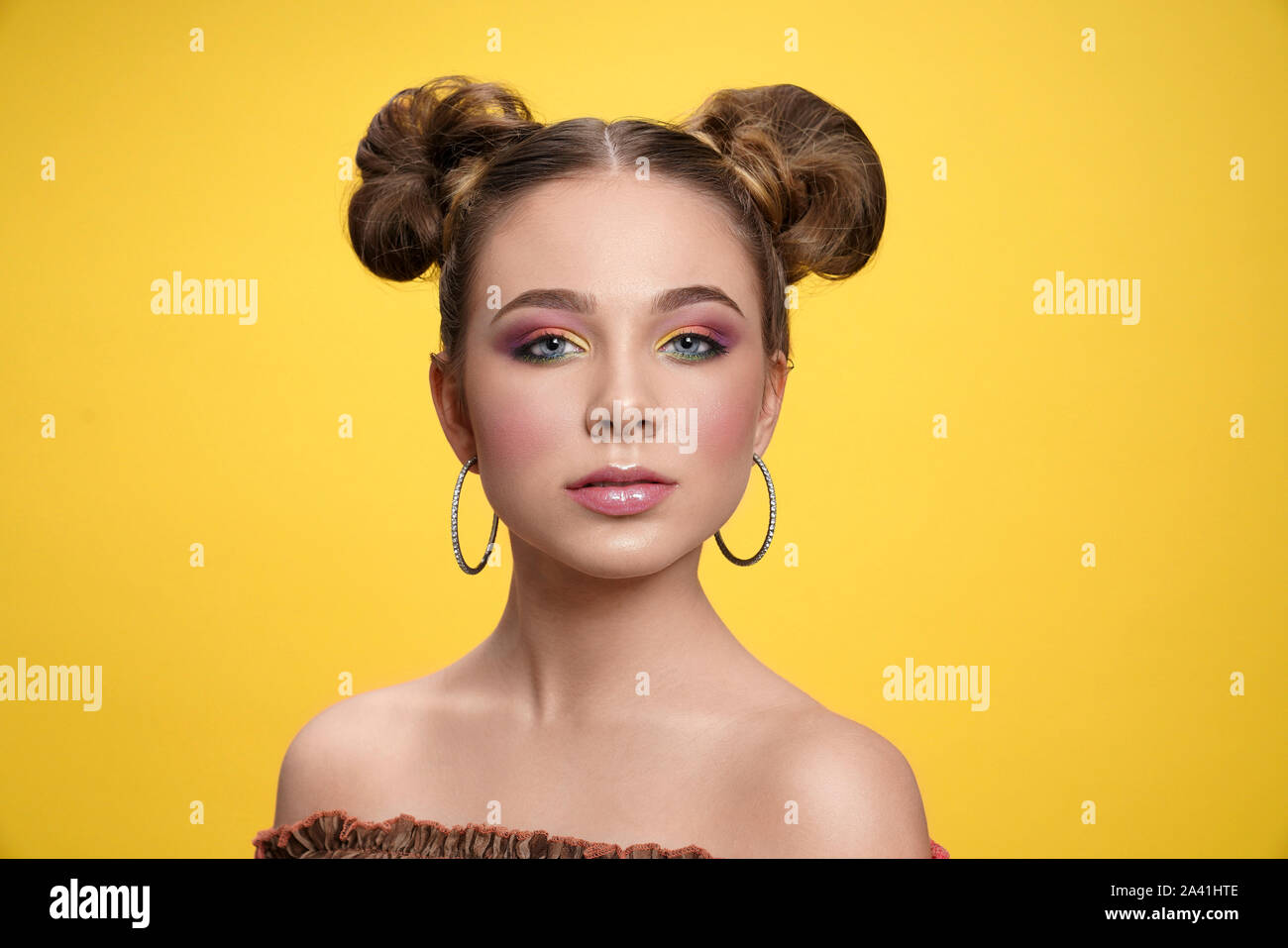 Vorderansicht des Ernstes Mädchen mit hellen Make-up und Schatten Kamera schaut im Studio. Weibliche Teenager tragen Ohrringe auf gelben Hintergrund posiert isoliert. Konzept der Trends und Stil. Stockfoto