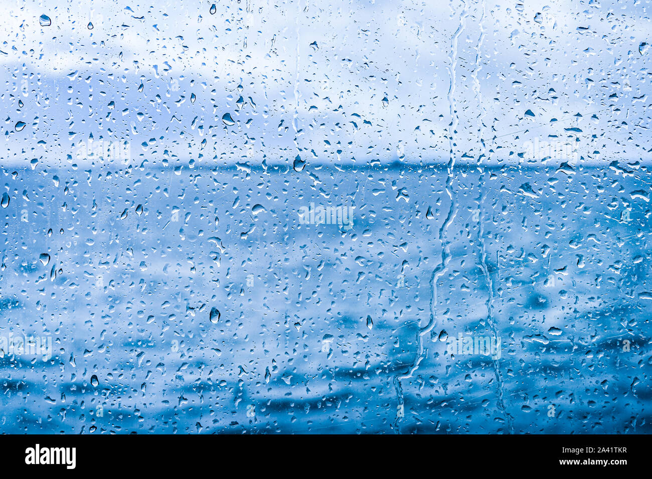 Wasser fällt auf Glas vor blauem Hintergrund ab Stockfoto