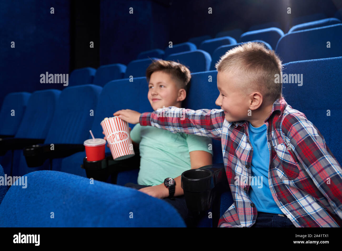 Seitenansicht der lustigen Jungen komischen Film gemeinsam im Kino. Little Boy in kariertem Hemd, lecker Popcorn von männlichen Freund. Kinder lachen aufliegt und an den Wochenenden. Konzept der Kindheit. Stockfoto
