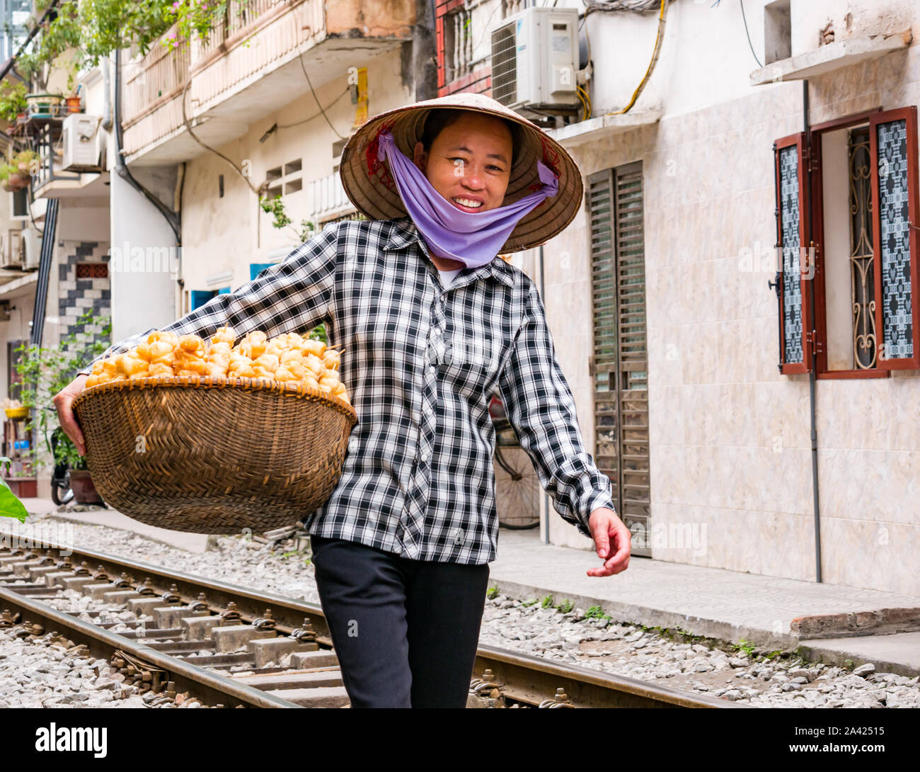 Lächelnd asiatische Frauen, Verkäufer Food Street tragen Vietnamesische konische Hut, zu Fuß auf den Gleisen in Railway Village oder Zug Street, Hanoi, Vietnam Stockfoto
