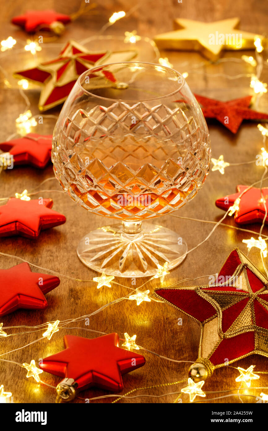 Crystal Schnaps Glas mit mit Weihnachtsbeleuchtung und roten Sternen Dekorationen, auf einem Holztisch Stockfoto