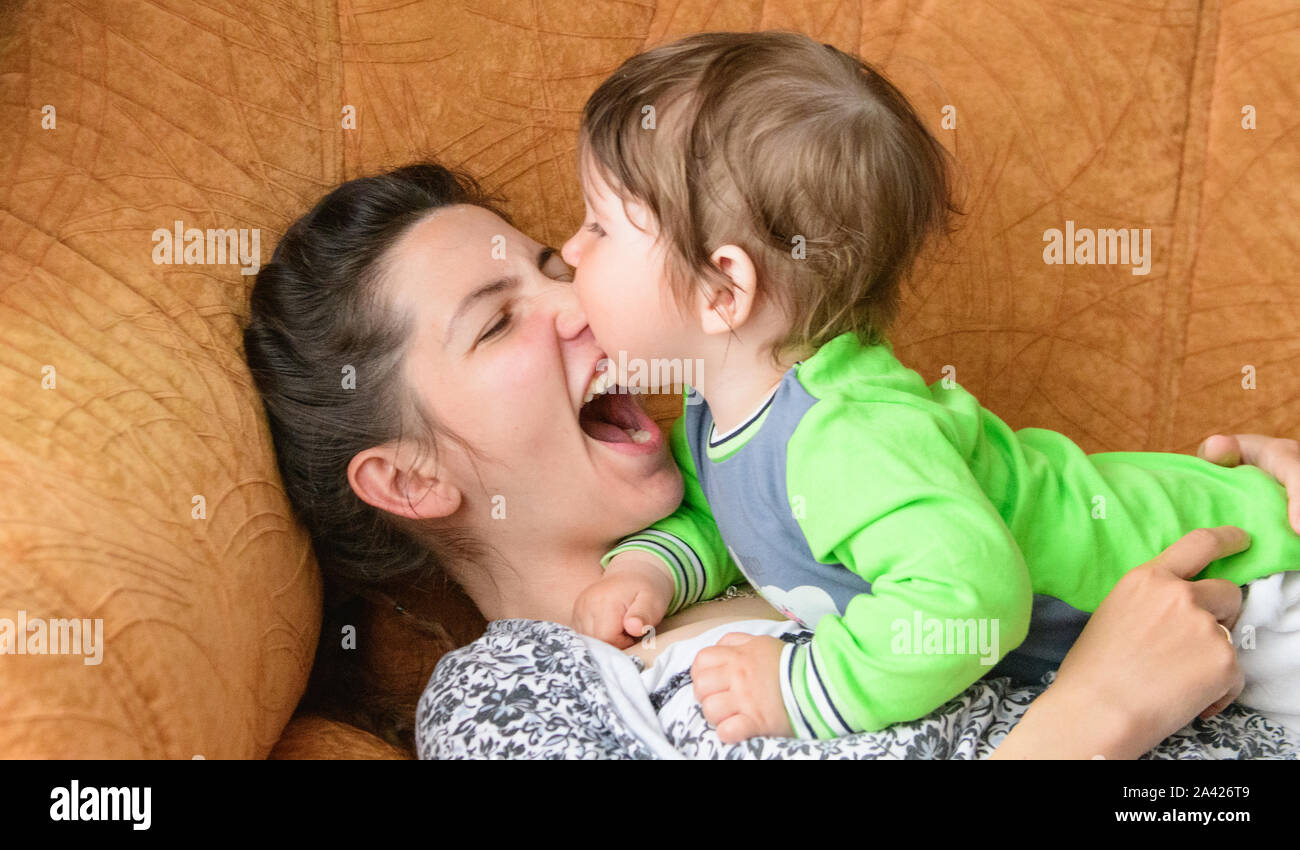 Baby beißt Mammen Nase. Glückliche Mutter mit Baby. Ein Junge beißt sich Mütter Nase auf der Couch. Spaß mit Ihrer geliebten Mutter Stockfoto