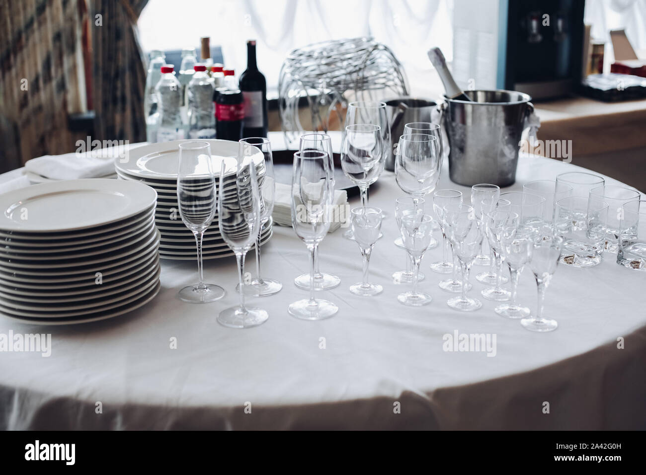 Blick über weiße runde Tisch mit Stapeln von weißen Platten, leere Champagnergläser und Gläser mit Flaschen Wasser und Eis Eimer. Stockfoto