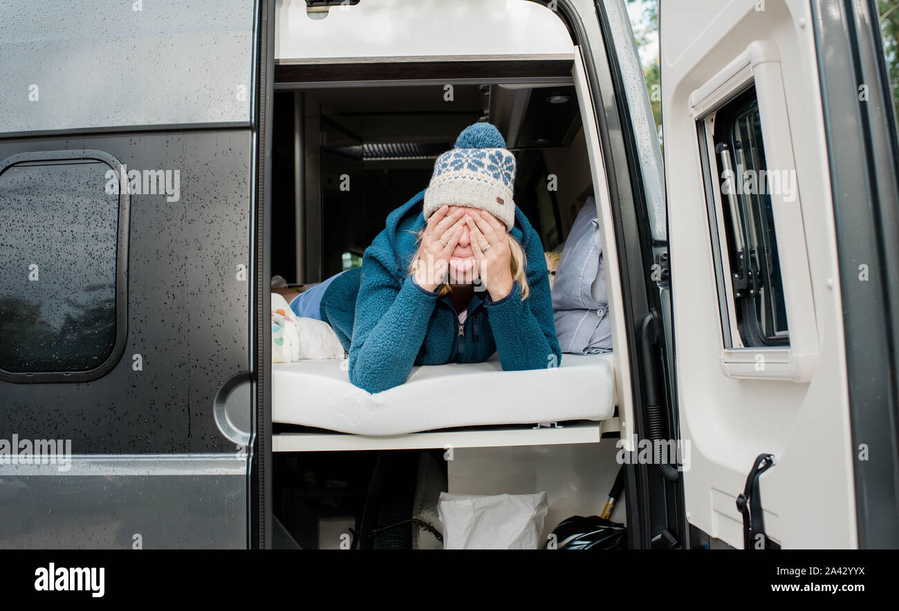 Blonde Frau verstecken ziehen dumme Gesichter in einem Wohnmobil camping Stockfoto