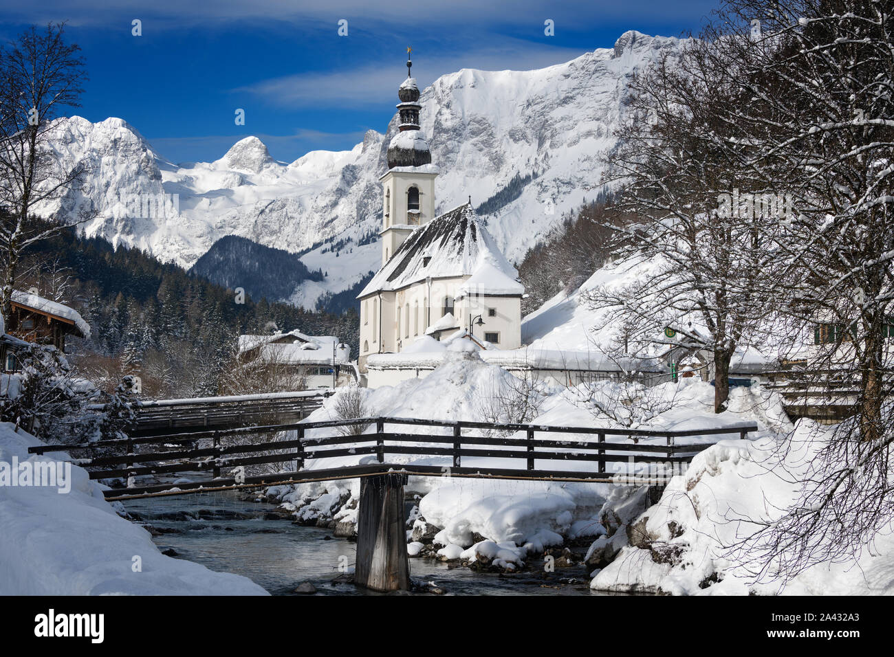 Kirche neben einem Bergbach mit Brücke und Alpengebirge, schneebedeckt in einer Landschaft in Ramsau bei Berchtesgaden, Deutschland. Stockfoto