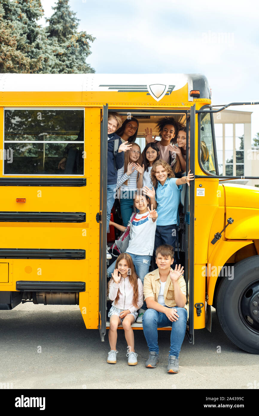 Mitschüler zur Schule mit dem Bus auf der Treppe sitzen zusammen Posieren winken fröhlich Stockfoto