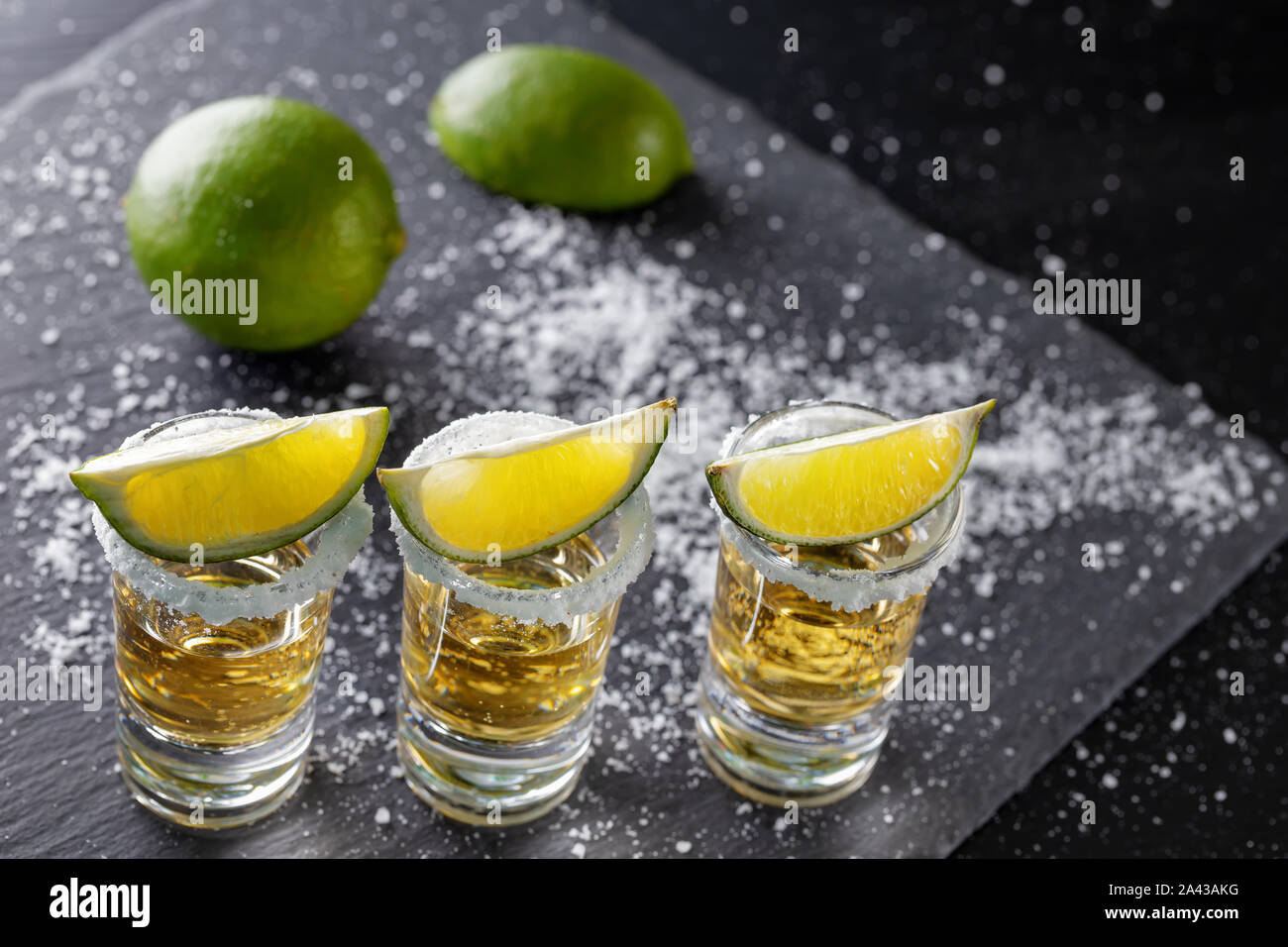 Drei Gläser golden Mexikanischen Tequila und Kalk mit Salz auf einem dunklen Hintergrund Stockfoto