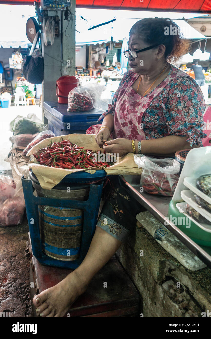 Chon Buri, Thailand - 16. März 2019: Nong Mon Markt. Sitzung Frau mit großen Gläsern reinigt Haufen von red chili peppers in Ihrem Fisch Verkauf stand. Stockfoto