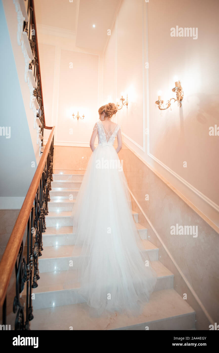 Ein Mädchen in einem Kleid klettert die Treppe hoch. Schöne Dame in einem luxuriösen Ballkleid die Treppen. Kunst Elemente Geländer auf beiden Seiten. Vintage Konzept Stockfoto