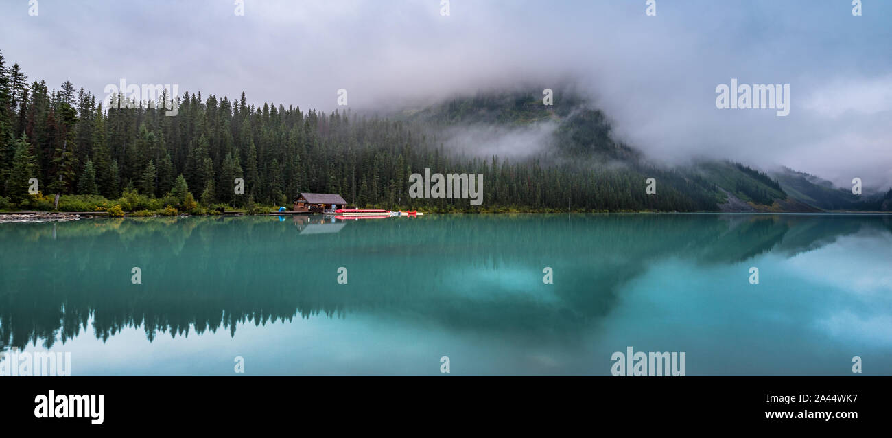 Malerischer Blick auf eine Kabine auf den türkisfarbenen Lake Louise mit Reflexionen über die umliegenden Berge an einem nebligen Tag, Banff National Park, Alberta Stockfoto