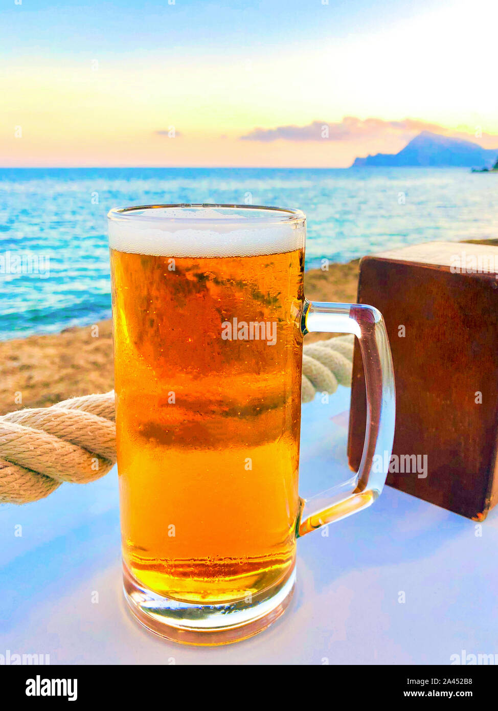 Ein erfrischendes Glas Bier bei Sonnenuntergang am Strand Stockfoto